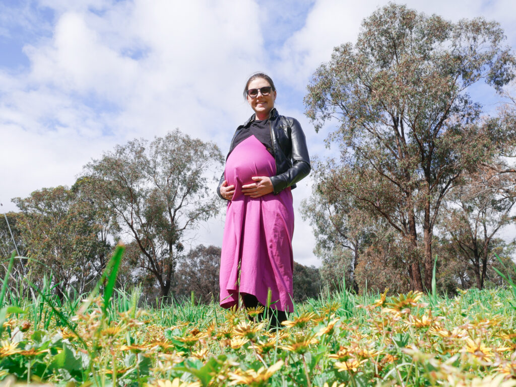 Jess standing in a field wearing a long pink dress and black leather jacket at 40 weeks pregnant
