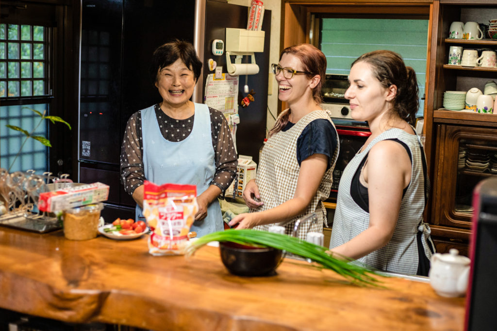 One of the Japanese hosts laughs with two guests in the kitchen as they prepare to make dinner together.