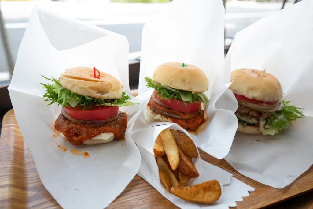 Three burgers lined up in a row with chips at one of Yunotsubo Kaido's restaurants, Yufuin Burger.