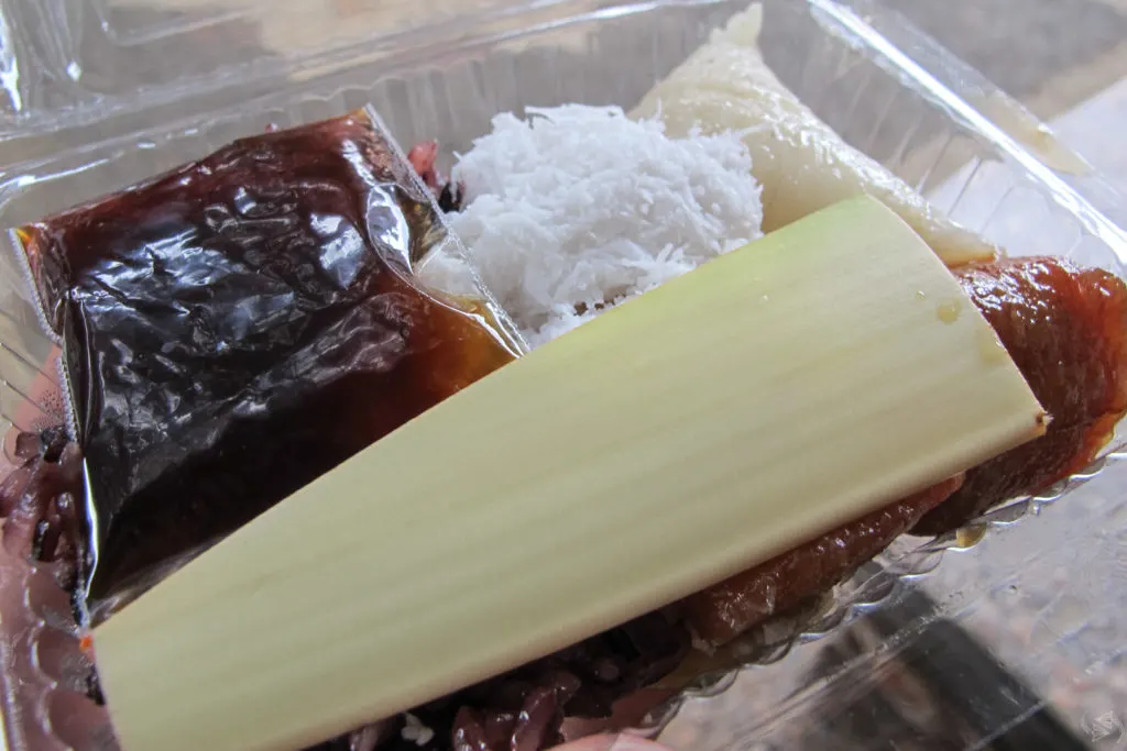 A variety of balinese sweets in a plastic container, including a bag of sugary syrup and a part of a plant to be used as a spoon.