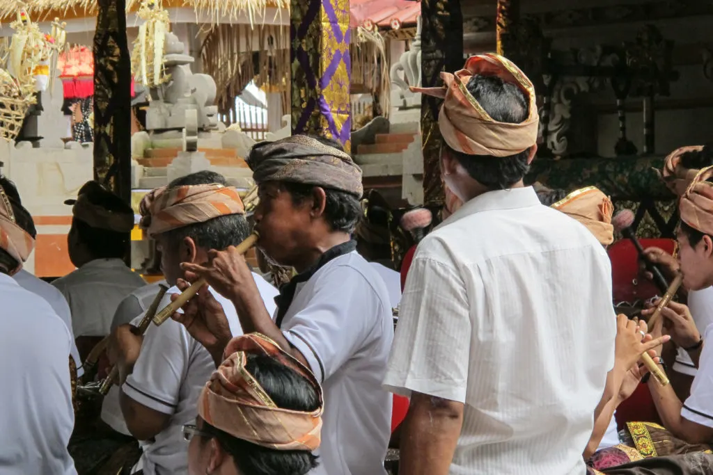 Local men wearing traditional headdresses play wooden recorder-like instruments.