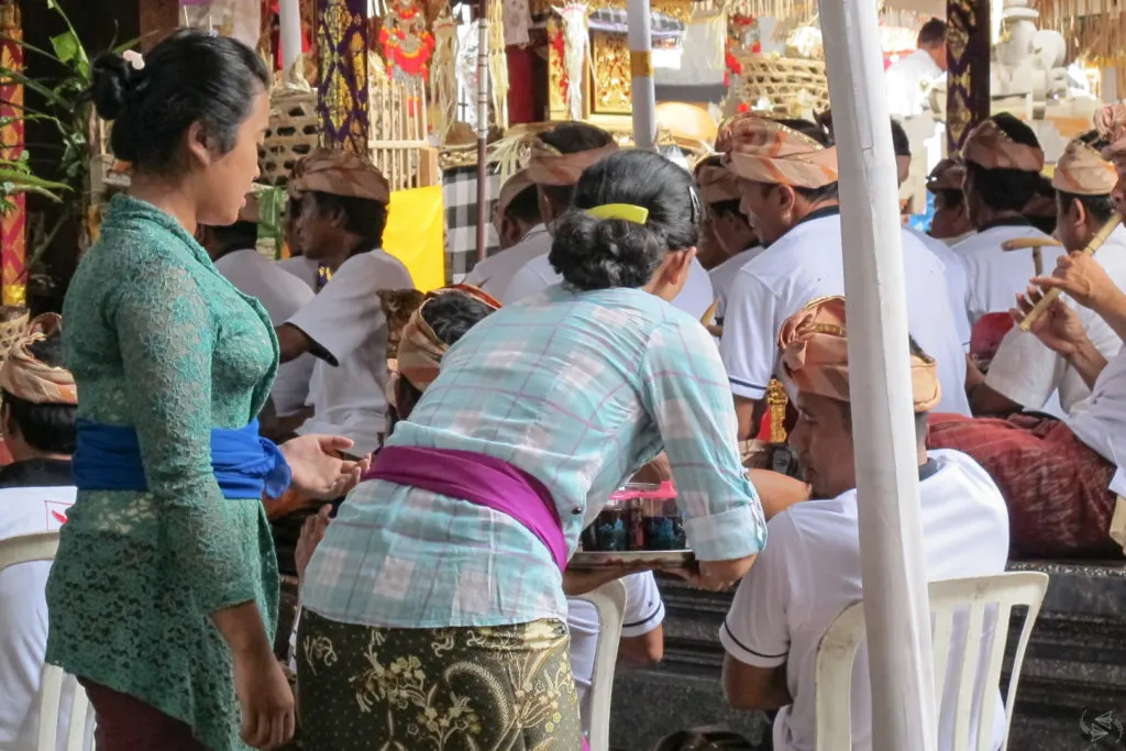 Women wearing traditional Balinese outfits serve coffee to the male musicians.