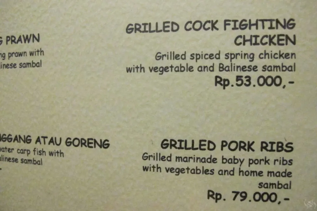 A photo of the restaurant menu that has 'Grilled Cock Fighting Chicken' on offer for 53,000 rupiah. The description of the dish says 'Grilled spiced spring chicken with vegetable and Balinese sambal'.