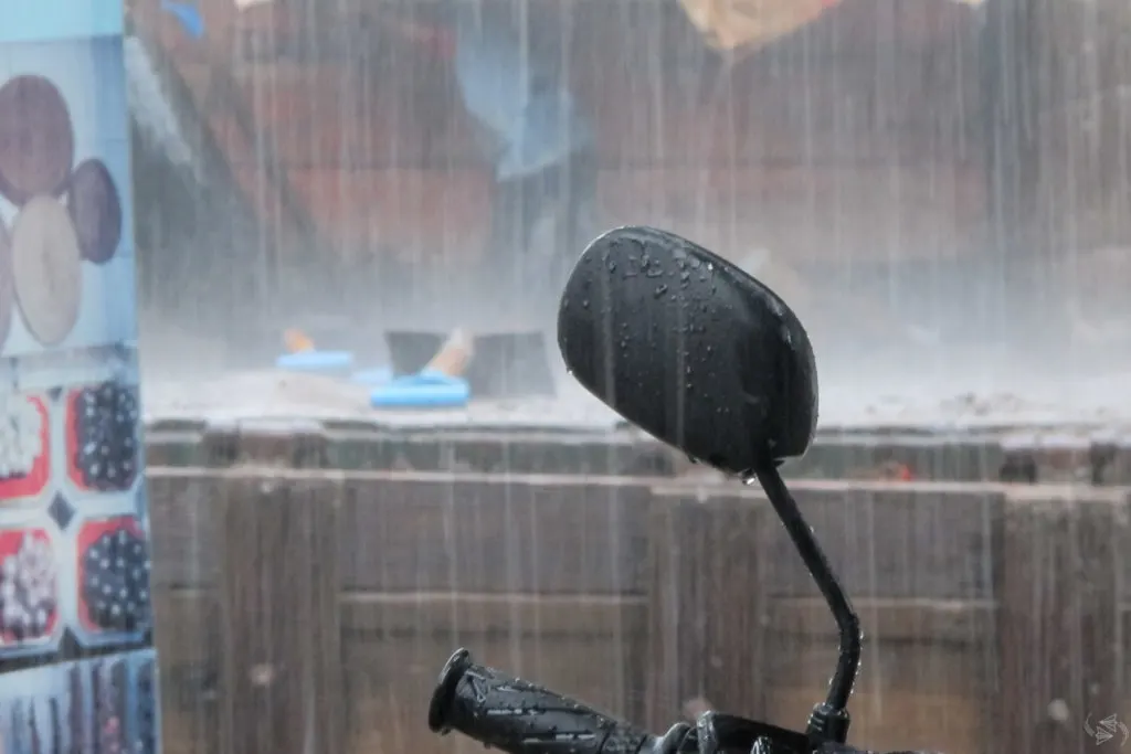 The rearview mirror of a scooter with torrential rain coming down all around.