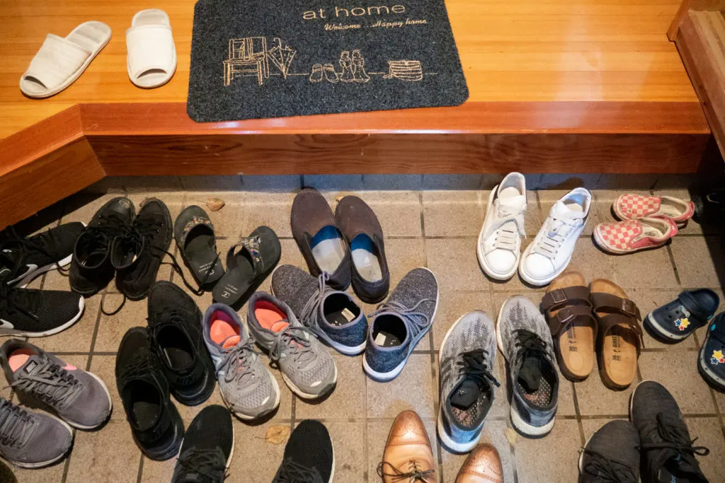 Japanese entrance way with lots of shoes on the lower part and a pair of inside slippers on the step up.