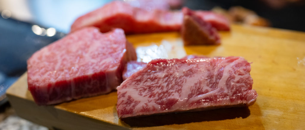 Marbled raw kobe beef steaks sit on a wooden chopping board.