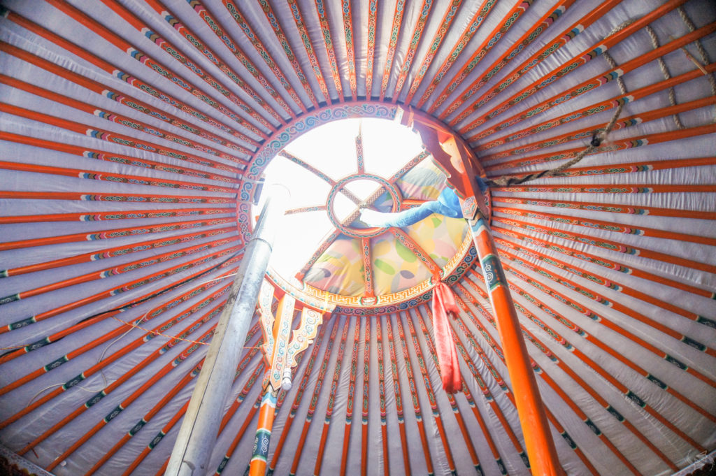 Looking up at the roof of a ger from the inside. The central portal is half open allowing sunlight to stream in.