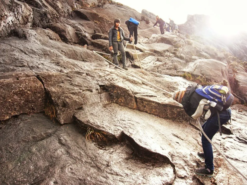 The author uses ropes to descend the steep rockface on the upper reaches of Mount Kinabalu, while the guide looks on.