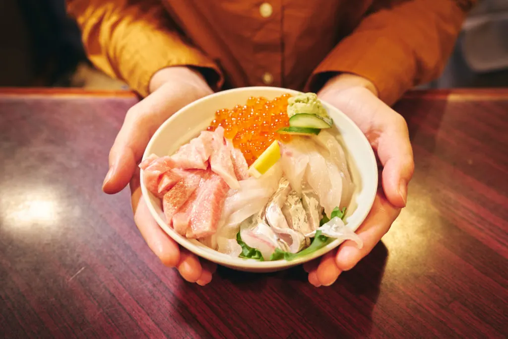 Woman cusps a rice bowl topped with fresh seafood and a generous amount of wasabi.