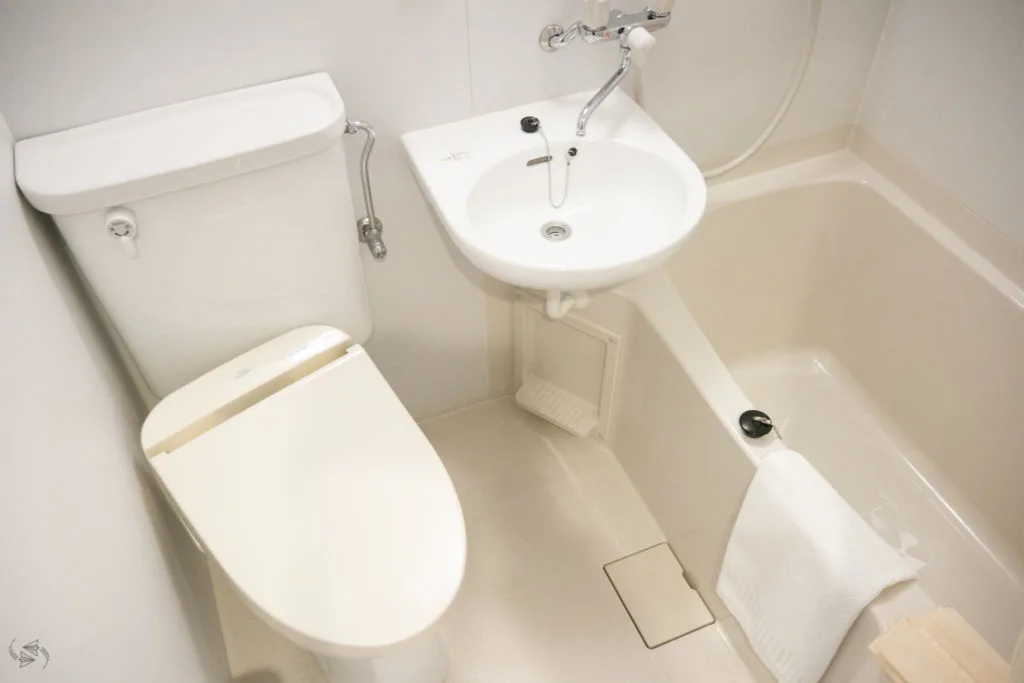 A small Japanese bathroom with the toilet, sink and bath tub all in the same room. The shower is over the bath. 