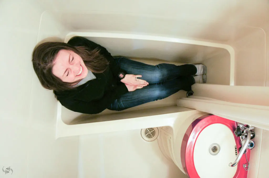 Author sits laughing in a tiny japanese bath tub, legs bent just to fit.