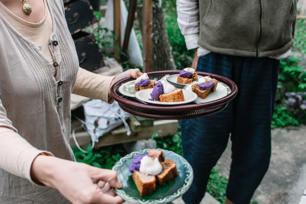 A woman holds out plates of cake with eye-catching white and purple topping.