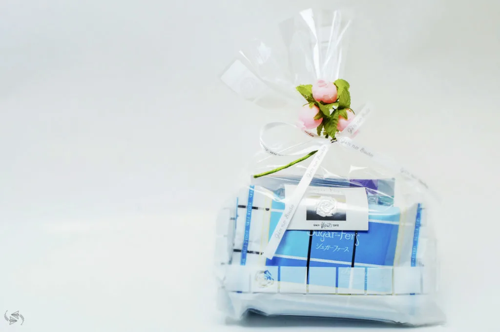 A White Day gift. Blue and white-packaged sweets inside a clear bag with a white ribbon and artificial pink flowers with green foliage to tie the bag up.