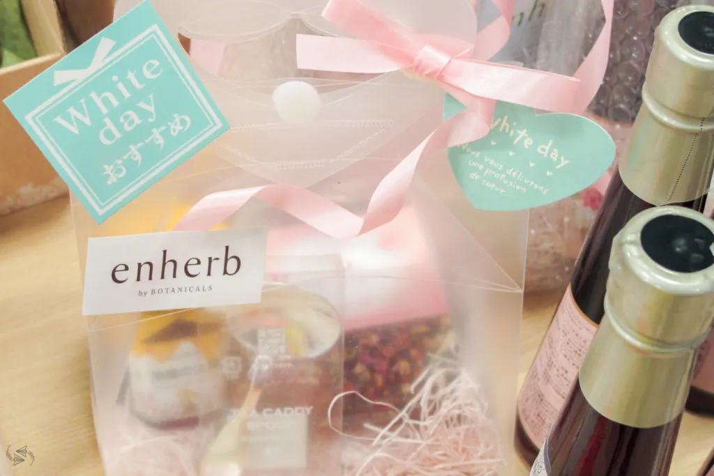 A French tea pack with high-end loose leaf tea and spoon in clear packaging with a pink bow sits on a shelf in a store in Tokyo with a tag that says it's recommended as a gift for White Day.